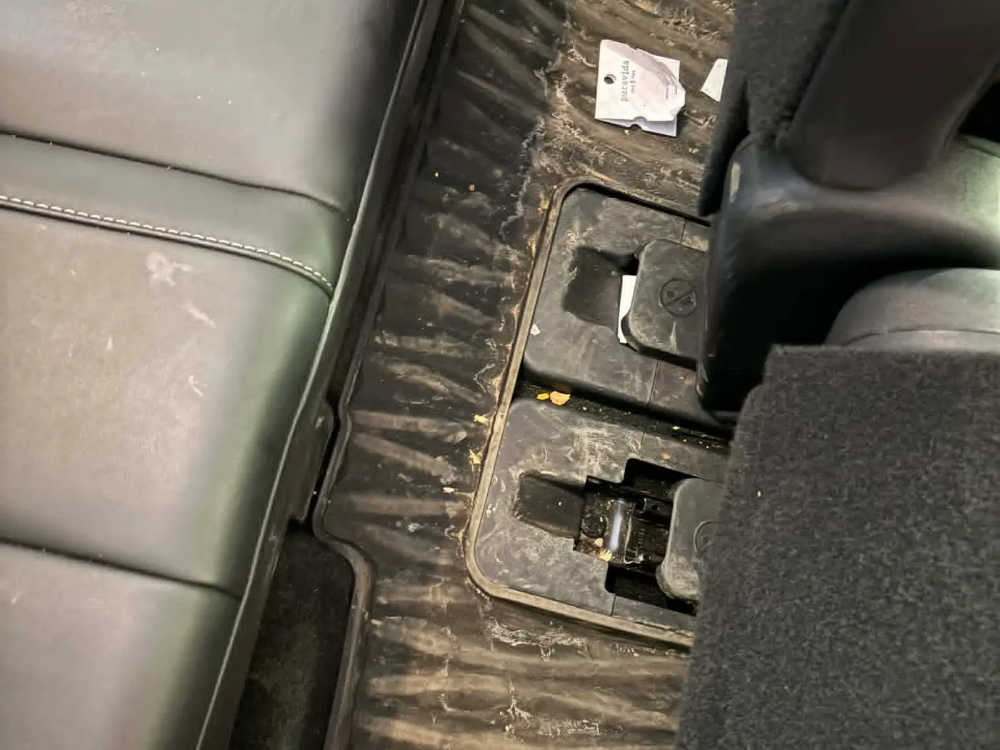 Rear footwell before detailing: carpet with dust, debris, and a stray tag